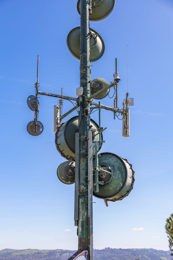 who-we-are Vertical shot of a communication tower with multiple satellite dishes against a clear blue sky.