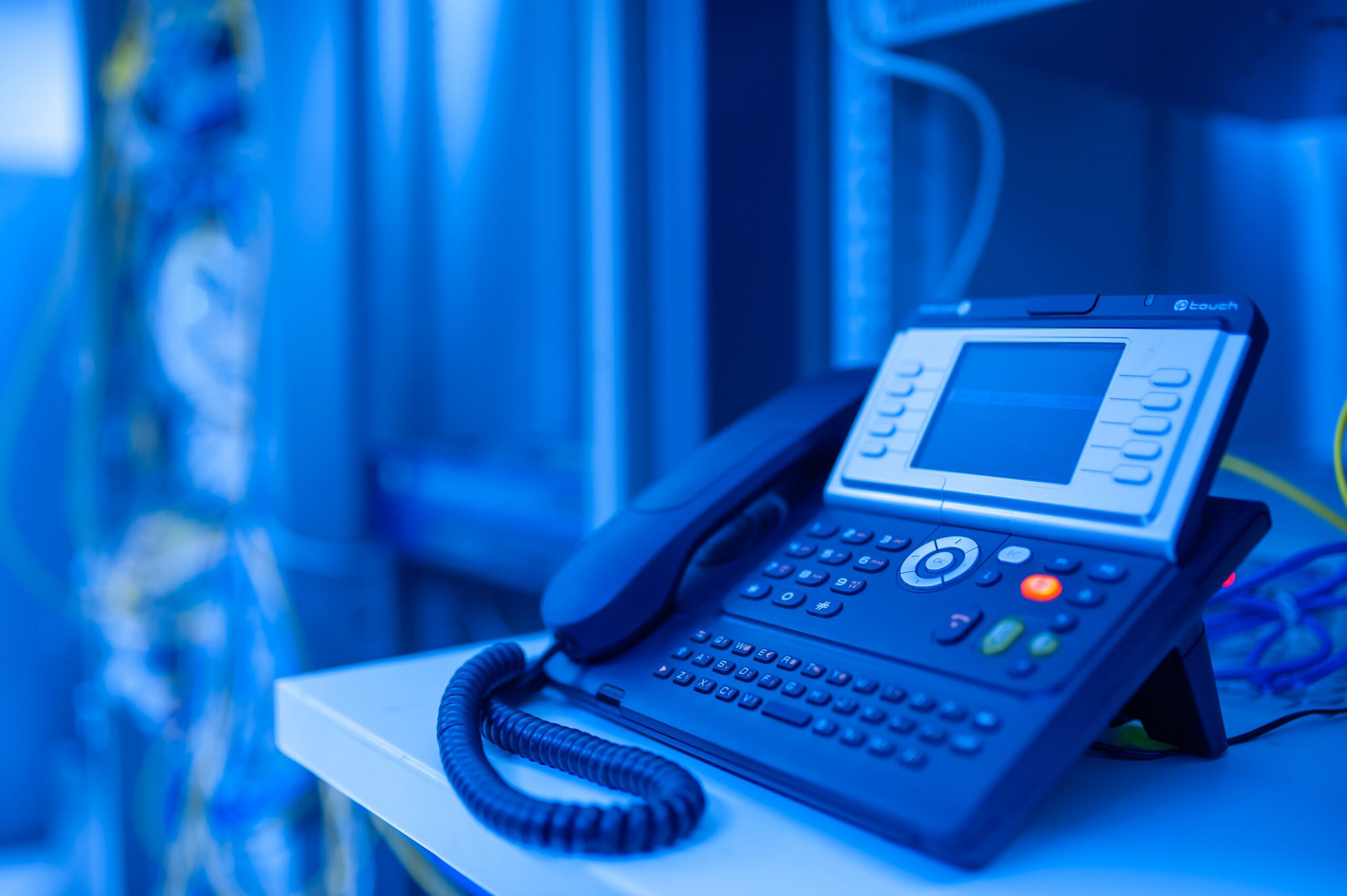 services-04 Close-up of a modern office phone in blue lighting. Ideal for tech and business themes.