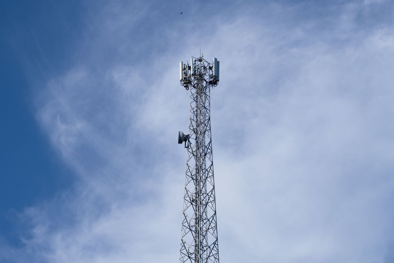 services-03 A tall metal communications tower stands against a backdrop of a clear blue sky with scattered clouds.